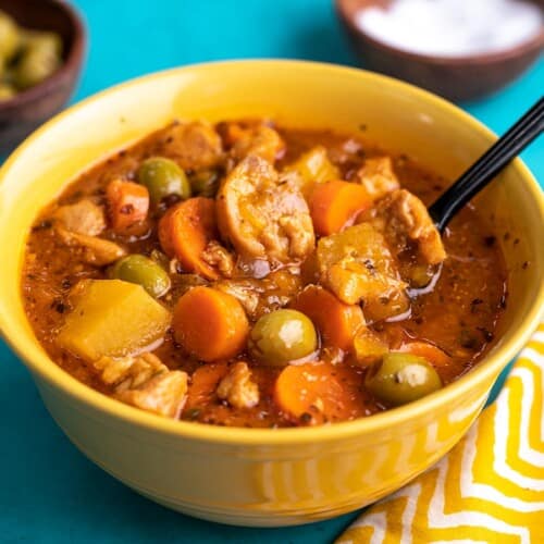 Side shot of Guisado de Pollo in a yellow bowl with a spoon in it.