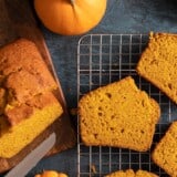 Overhead shot of sliced pumpkin bread with two mini pumpkins next to it on a dark background.
