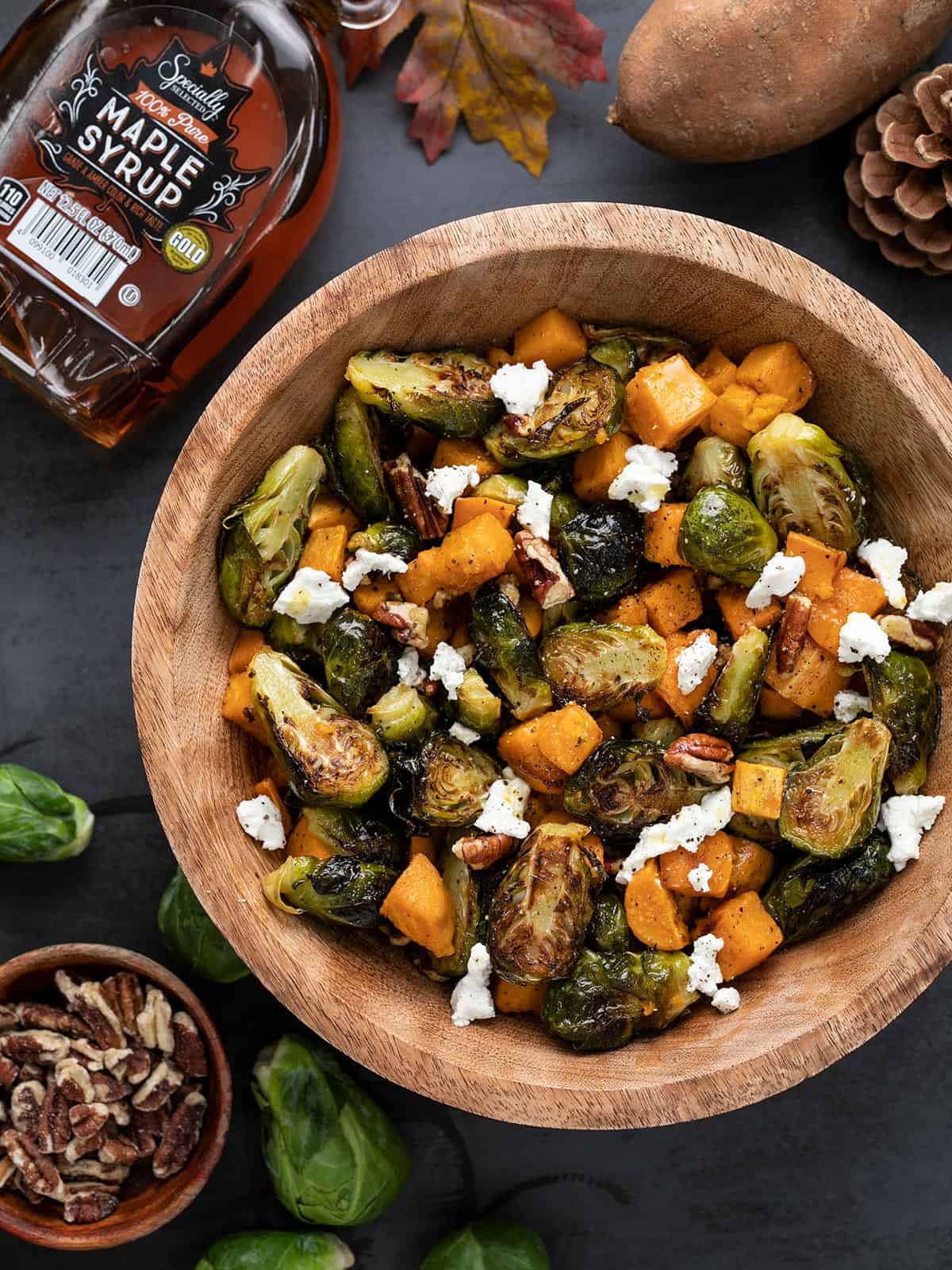 Overhead view of a wooden bowl full of roasted Brussels sprouts salad with ingredients on the sides.