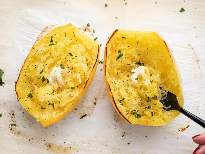 Overhead shot of roasted spaghetti squash dressed with butter and chopped Italian parsley with a fork in it.
