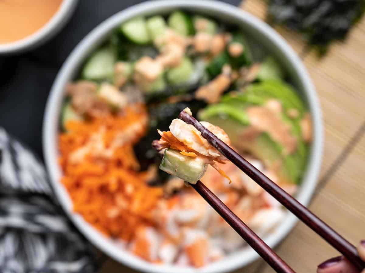 Close up of a bite of sushi bowl being held by chopsticks.