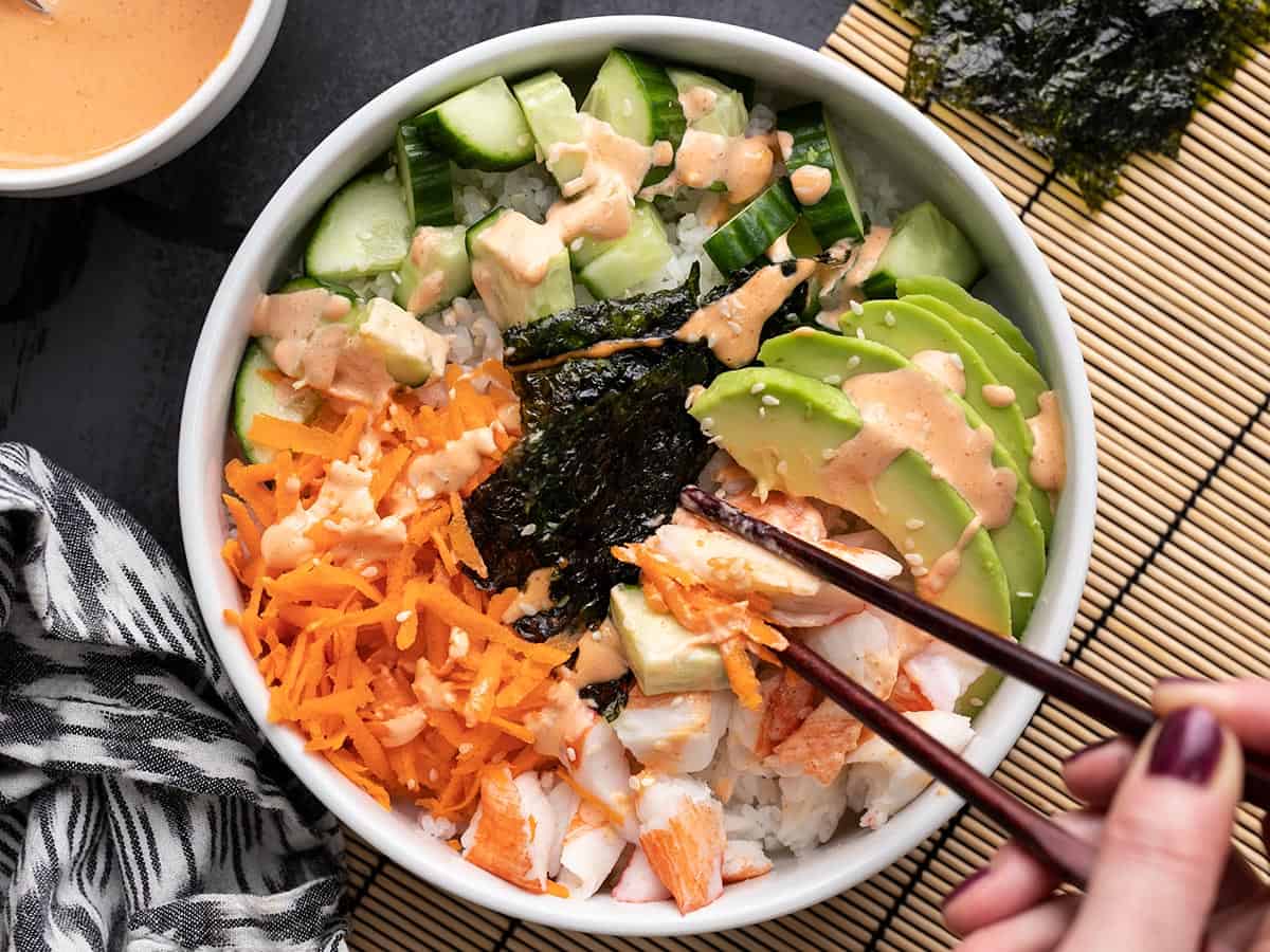 Overhead view of a sushi bowl being eaten with chopsticks.