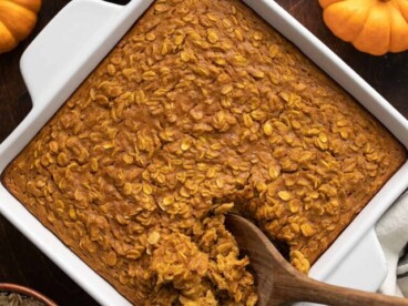 Overhead view of baked pumpkin pie oatmeal in the baking dish being scooped with a wooden spoon.