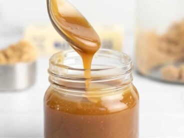 Side shot of a spoon drizzling caramel sauce in a mason jar.