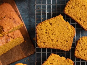 Overhead shot of sliced pumpkin bread with two mini pumpkins next to it on a dark background.