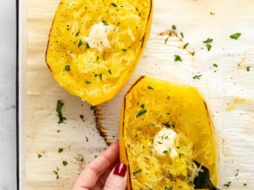 Overhead shot of hand holding cooked spaghetti squash dressed with butter and Italian Parsley. with a fork in it