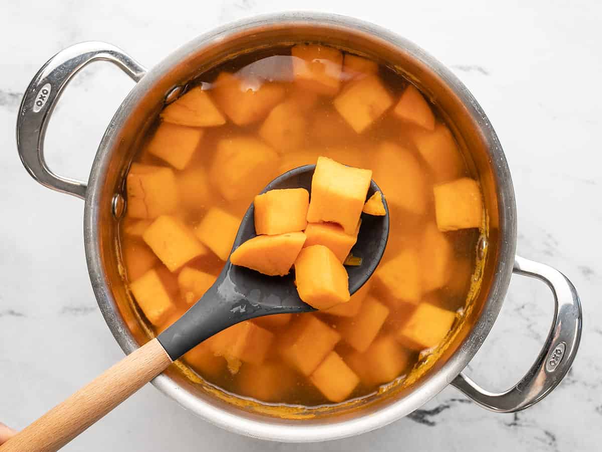 Overhead shot of a pot with boiled sweet potatoes in it with a serving spoon holding a few cubes of sweet potato above it.