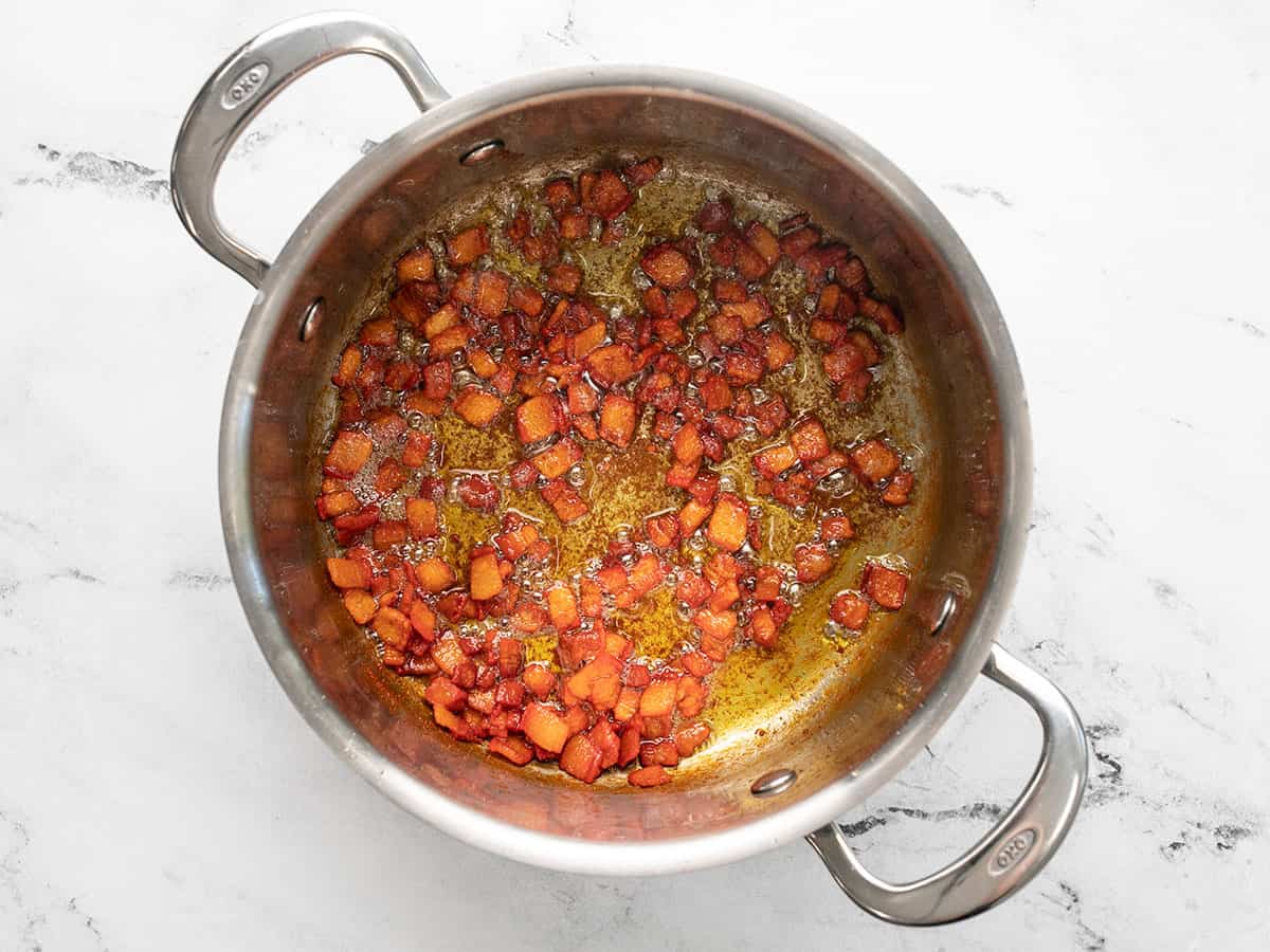 Overhead shot of salt pork frying in a silver pot.