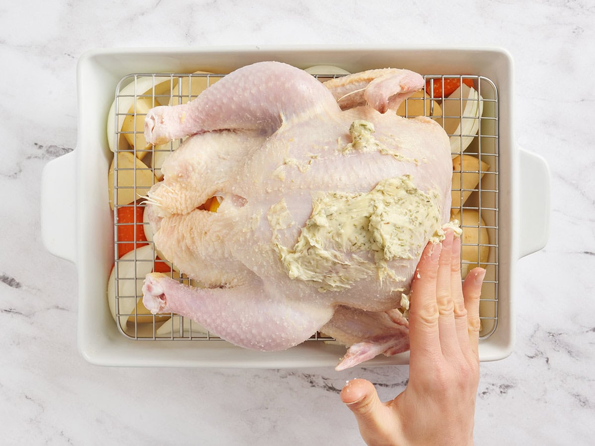 A whole chicken being rubbed with seasoned butter.