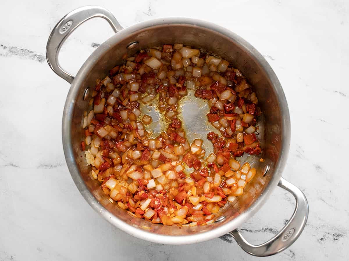 Overhead shot of salt pork, onions, and garlic, frying in a silver pot.