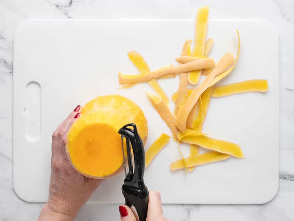 Butternut squash being peeled with a vegetable peeler.