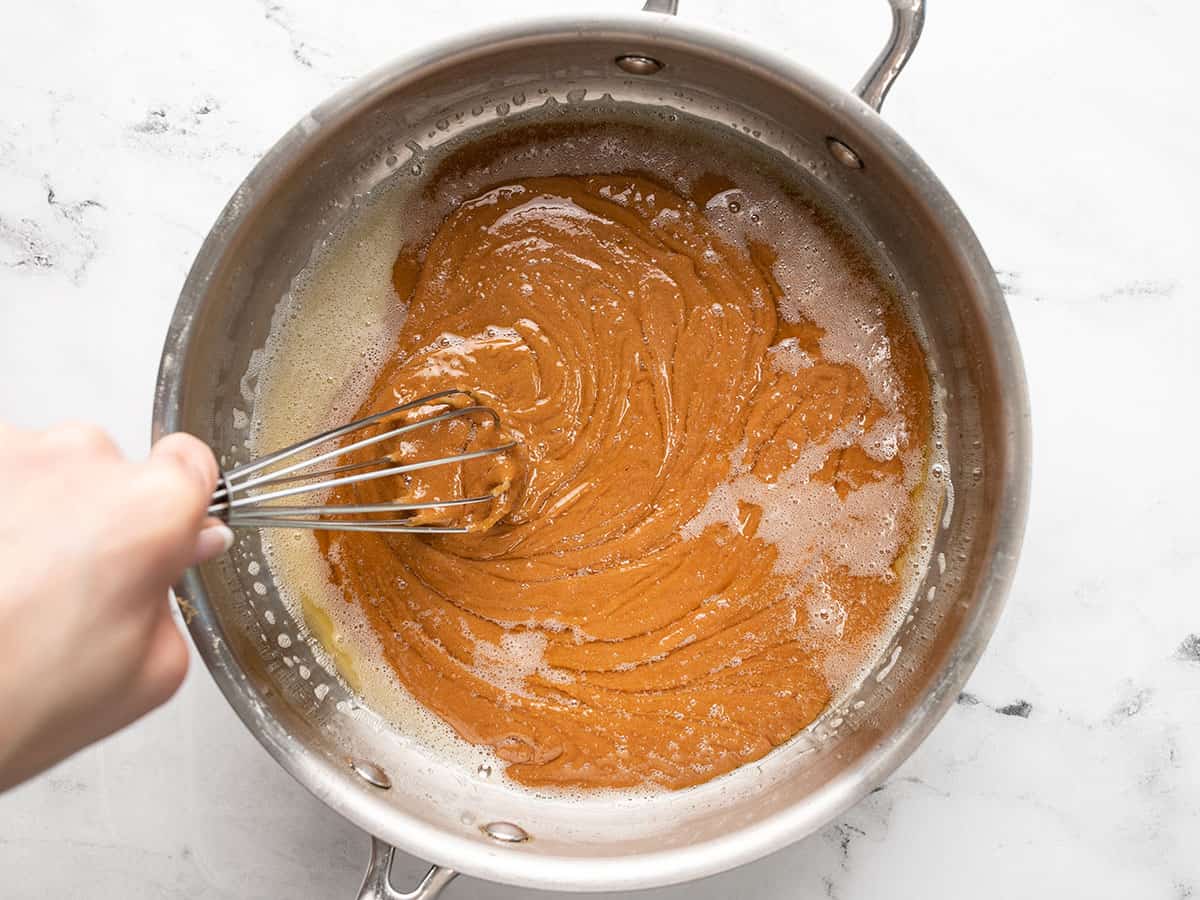 Overhead shot of hand mixing caramel in a pot with a whisk.