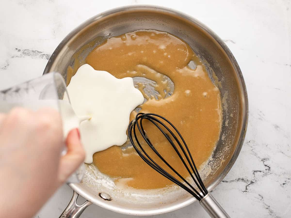 Overhead shot of cream v=being poured into a silver pan with caramel and a whisk in it.