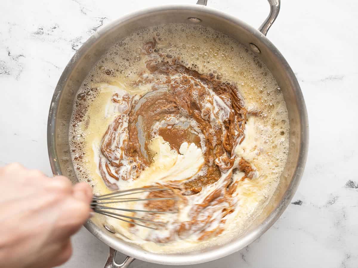 Overhead shot of hand mixing caramel and cream in a pot with a whisk.