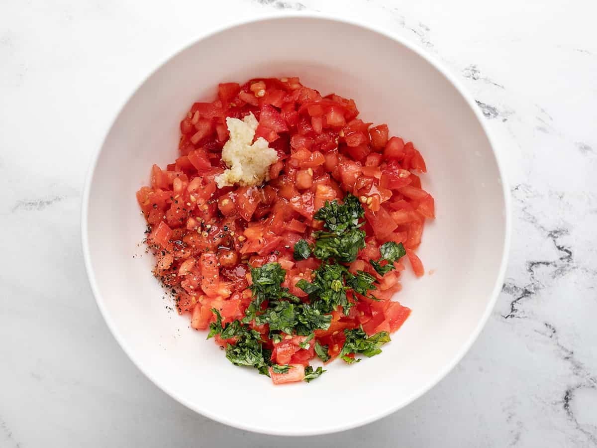 Overhead shot fo a white bowl with chopped tomatoes, basil, and minced garlic.