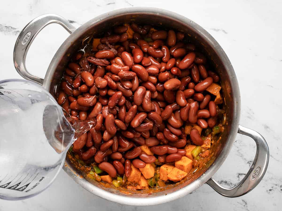 Overhead shot of water being added to a silver pot full of red beans.
