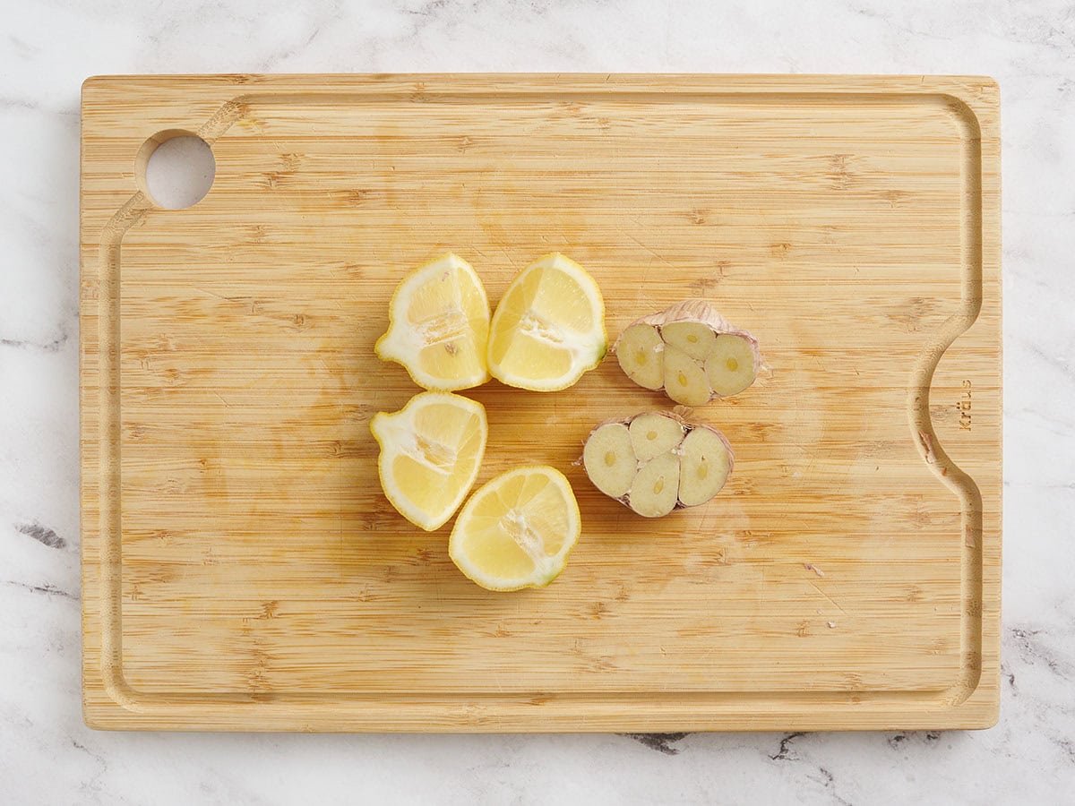 Lemon and a head of garlic sliced in half on a wooden cutting board.