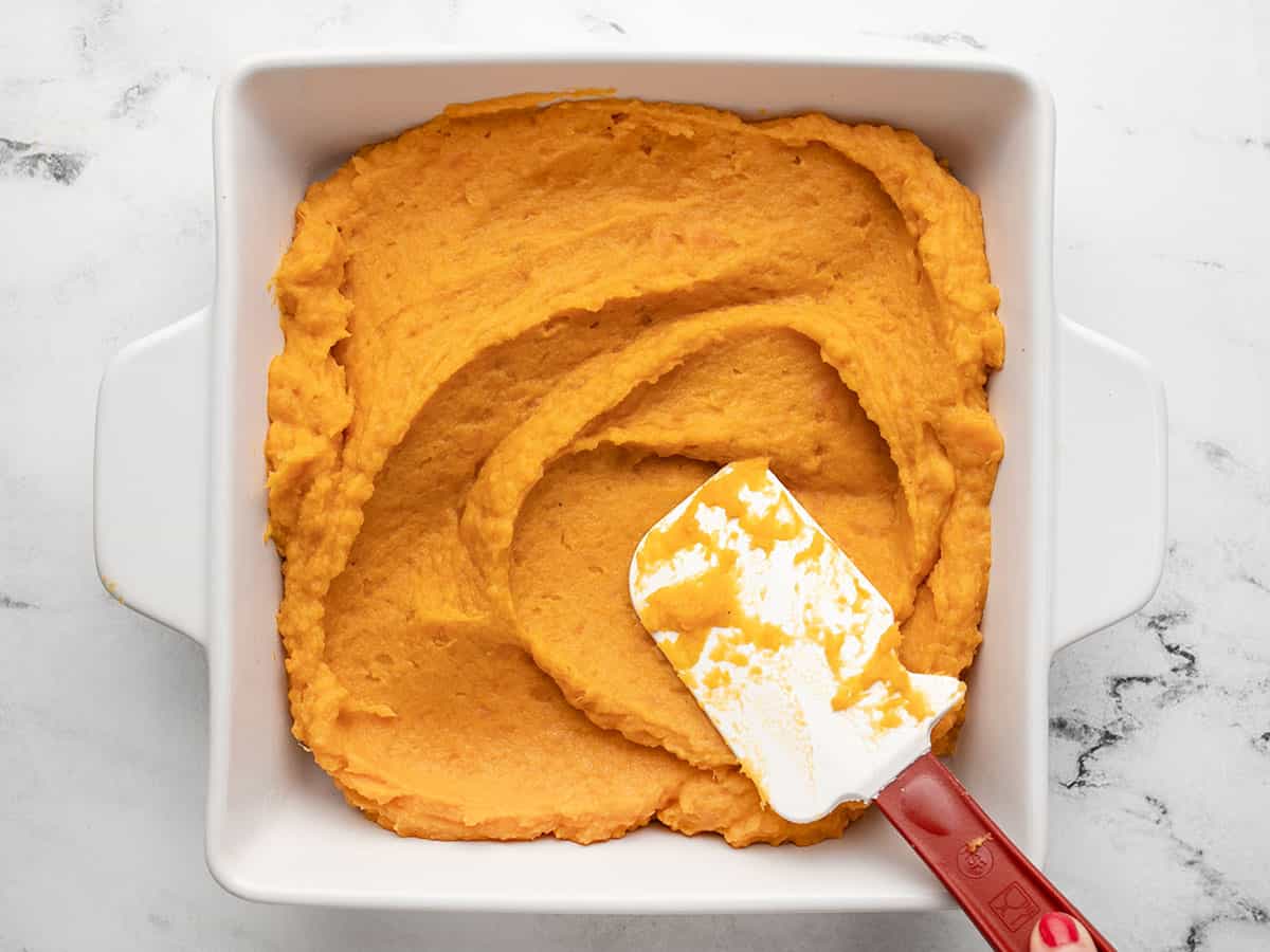 Overhead shot of a rubber spatula smoothing sweet potato casserole in a white casserole dish.