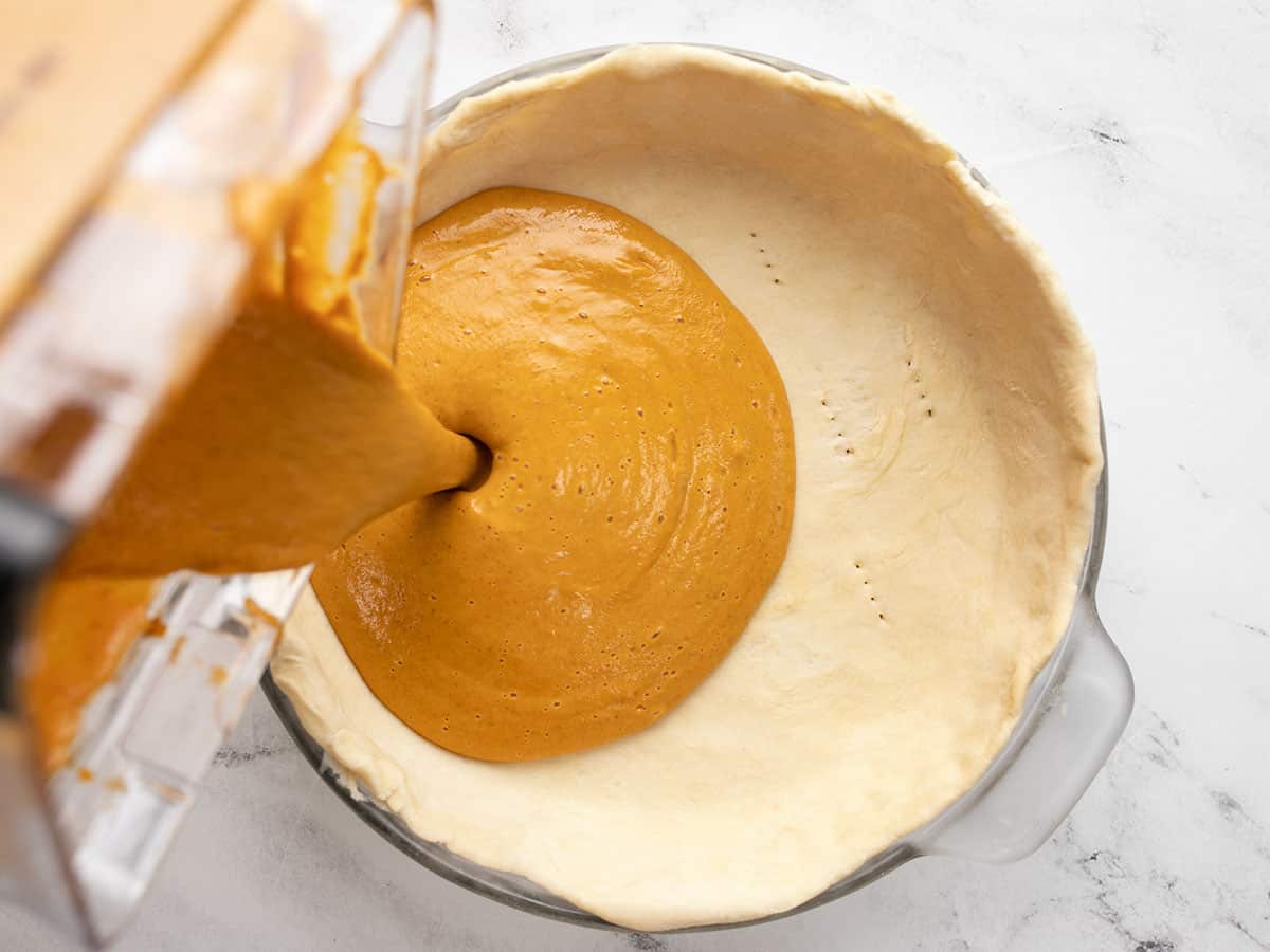 Pumpkin pie filling being poured into a pie crust.