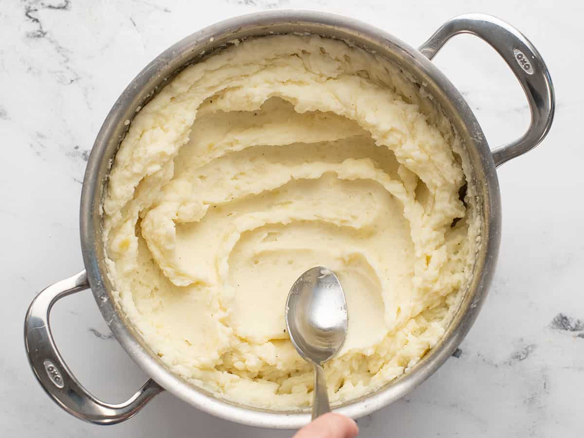 Finished mashed potatoes in the pot being smoothed with a spoon.