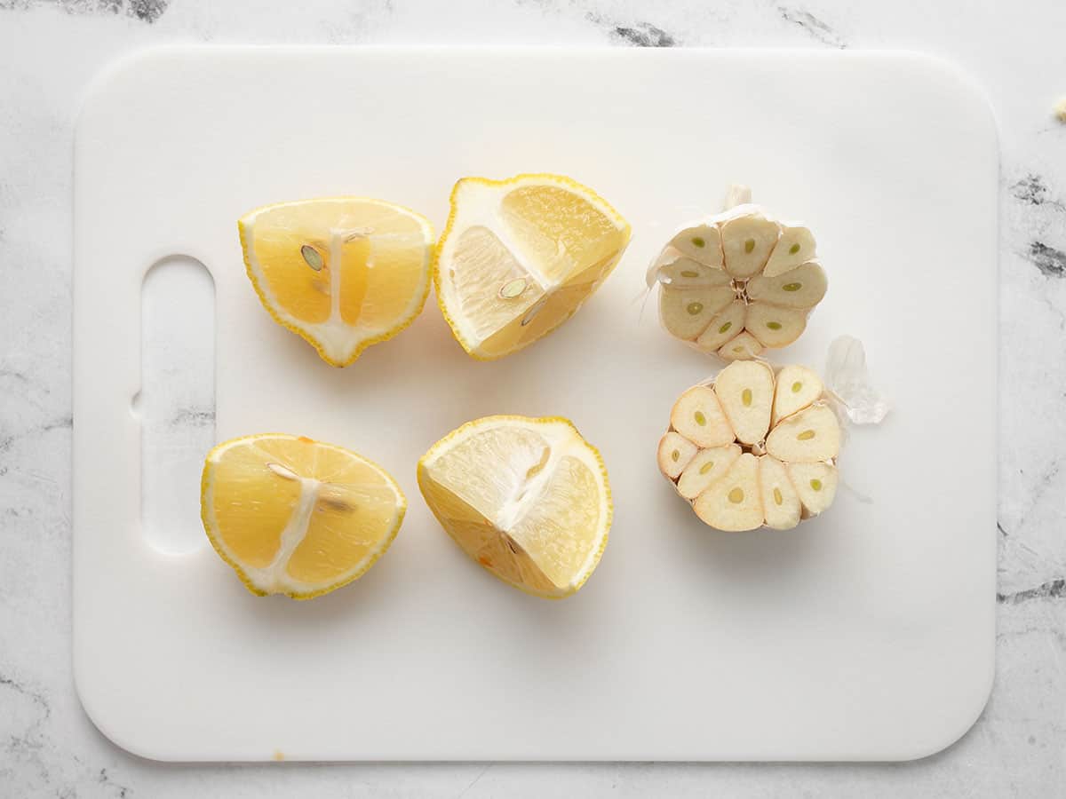 Overhead shot of a quartered lemon and a sliced head of garlic on a white cutting board.