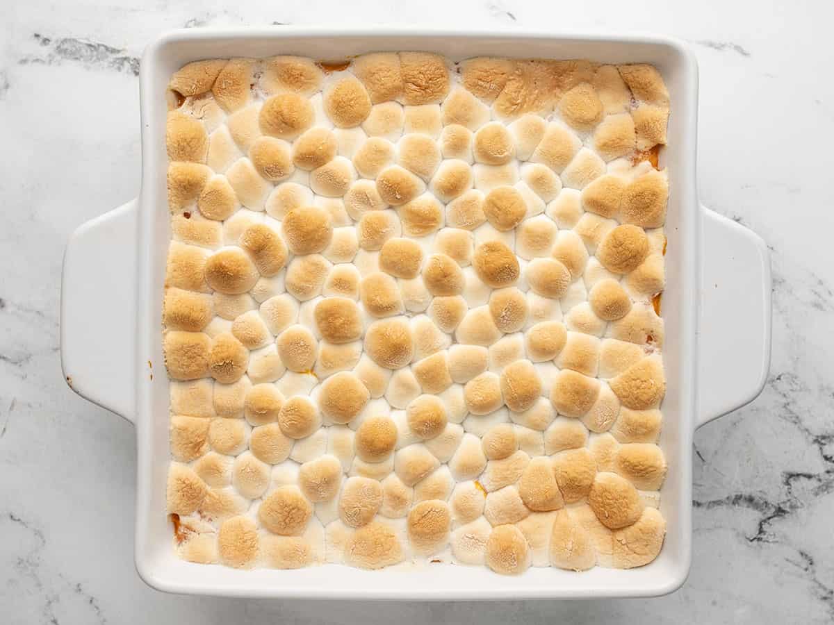 Overhead shot of sweet potato casserole in a white casserole dish with a silver serving spoon scooping out a bit of it.