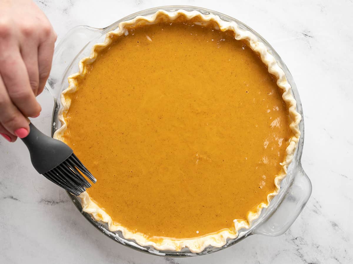 Heavy cream being brushed onto the crust of a pumpkin pie. 