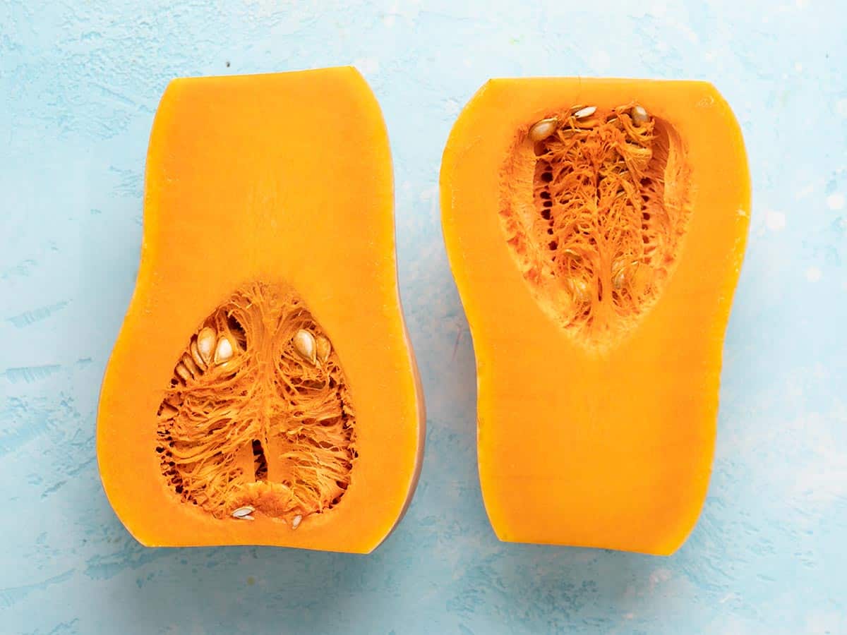 A butternut squash cut in half lengthwise with the insides exposed.