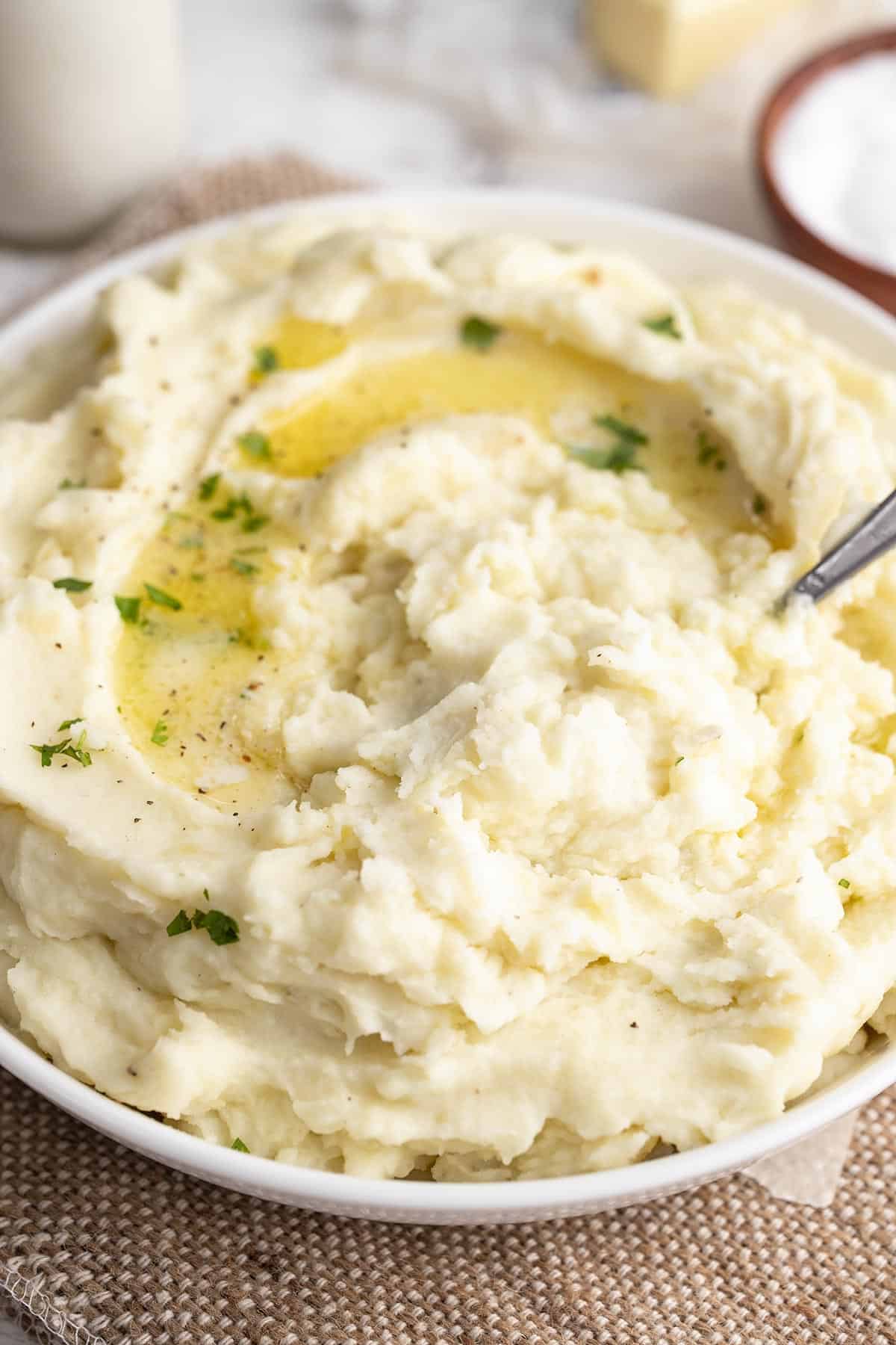 Close up side view of a bowl of mashed potatoes with melted butter and a spoon.