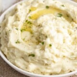 Close up side view of a bowl of mashed potatoes with melted butter.