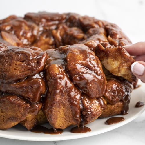 Side shot of hand pulling a piece of monkey bread out of a loaf.