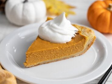 Side shot of a slice of pumpkin pie with a dollop of whipped cream on top of it.