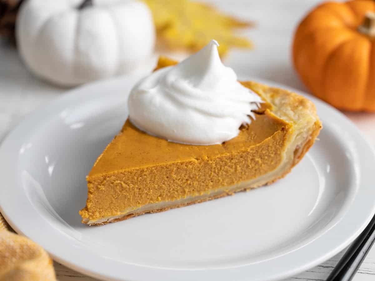 Side view of a slice of pumpkin pie on a plate with whipped cream. 