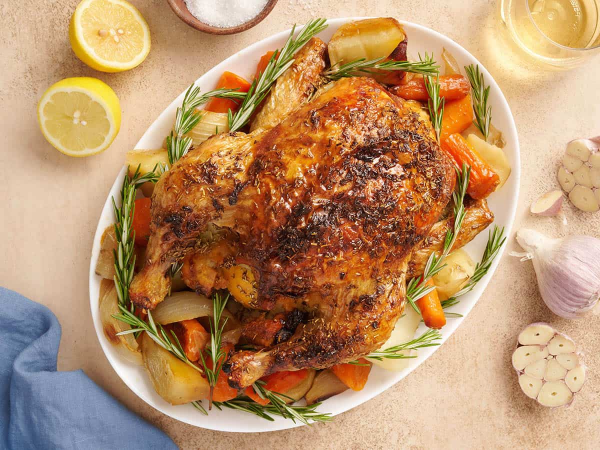 A whole oven roasted chicken on a platter with vegetables.