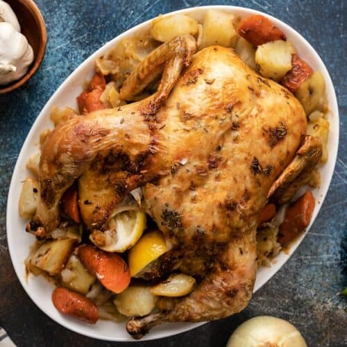 Overhead shot of whole roasted chicken and roasted vegetables on a white platter..