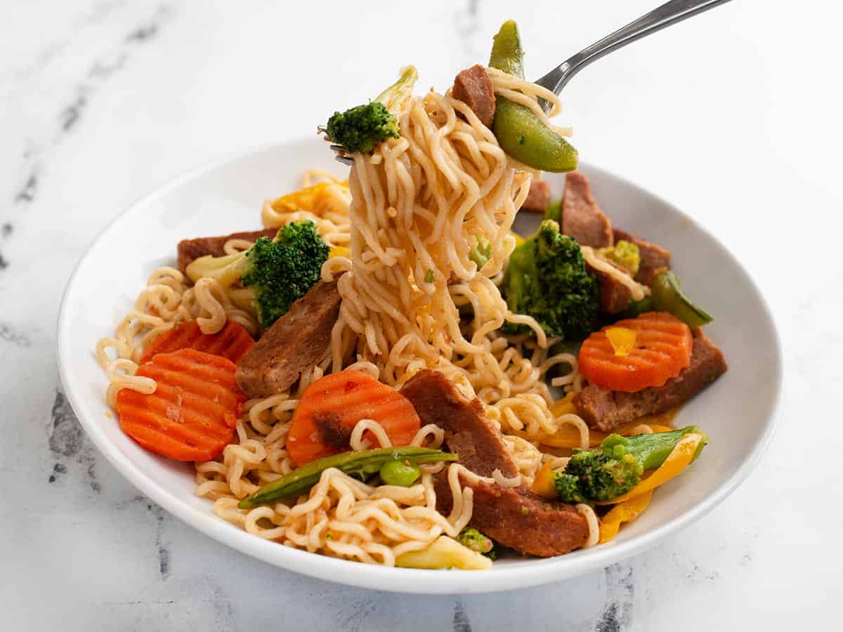 Side view of a bowl of spam stir fry noodles being lifted by a fork.
