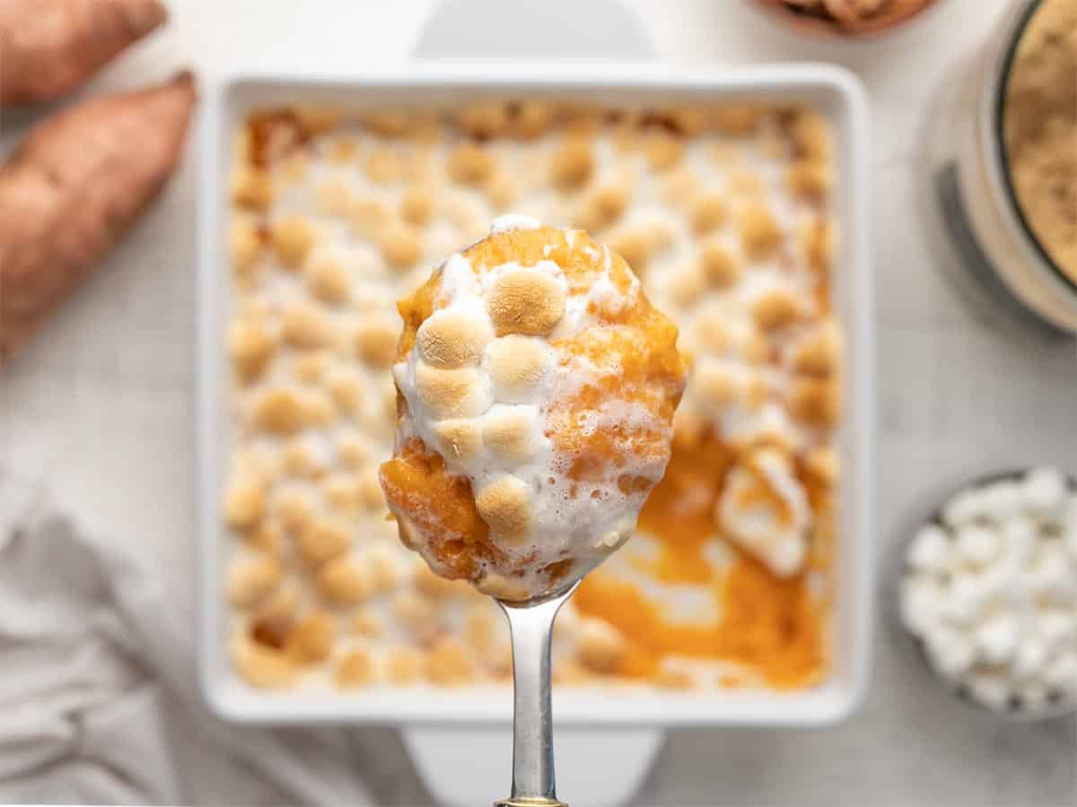Overhead shot of a sweet potato casserole in a white casserole dish with a silver serving spoon above it holding a spoonful of casserole.