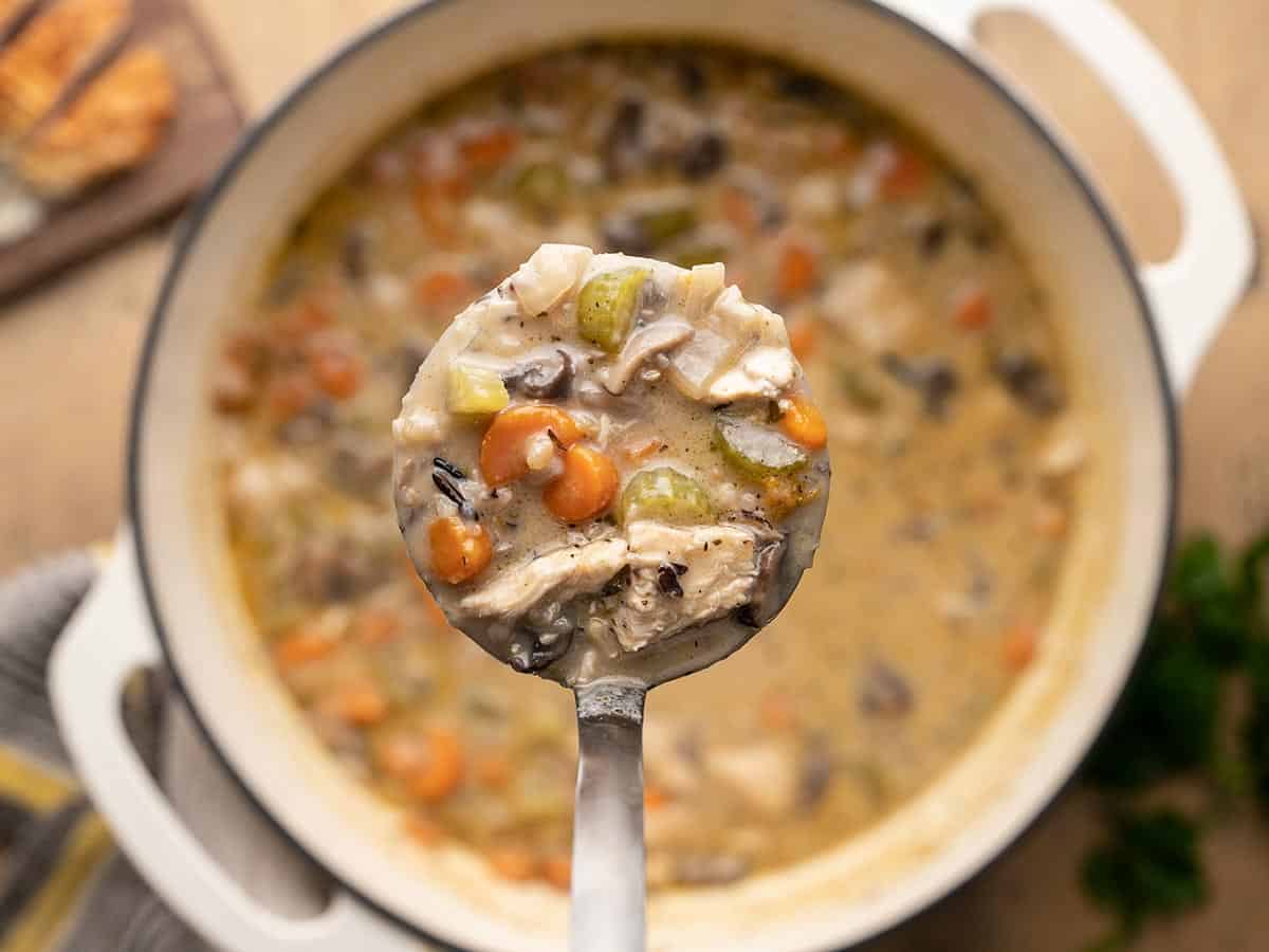 Close up of a ladle full of turkey and wild rice soup over the pot. 