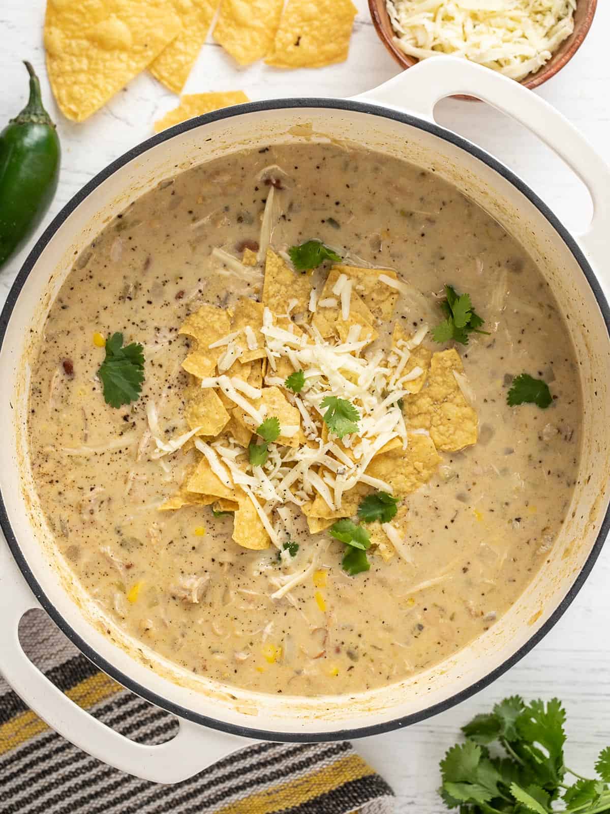 White chicken chili in the pot topped with cheese, tortilla chips, and cilantro.