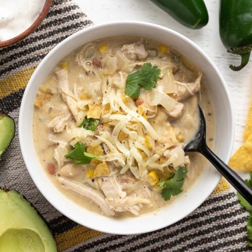 Overhead view of a bowl of creamy white chicken chili with toppings and a spoon.
