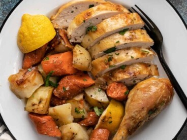 Overhead shot of sliced chicken and roasted vegetables on a white plate.
