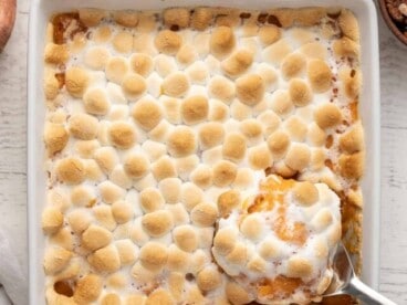 Overhead shot of sweet potato casserole in a white casserole dish with a silver serving spoon scooping out a bit of it.