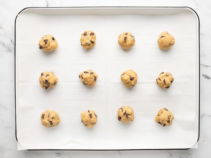 Overhead shot of cookie dough balls on a sheet pan lined with parchment paper.