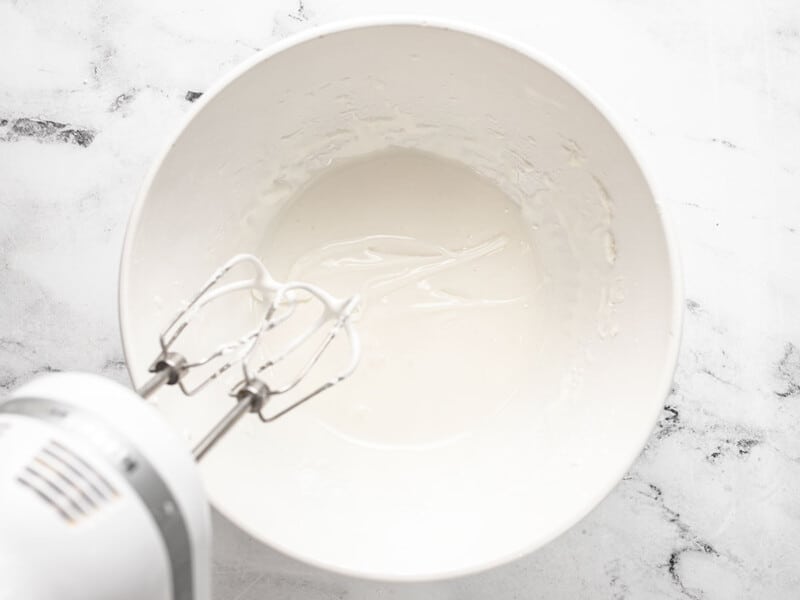 Overhead shot of icing being mixed with a hand blender in a white bowl.