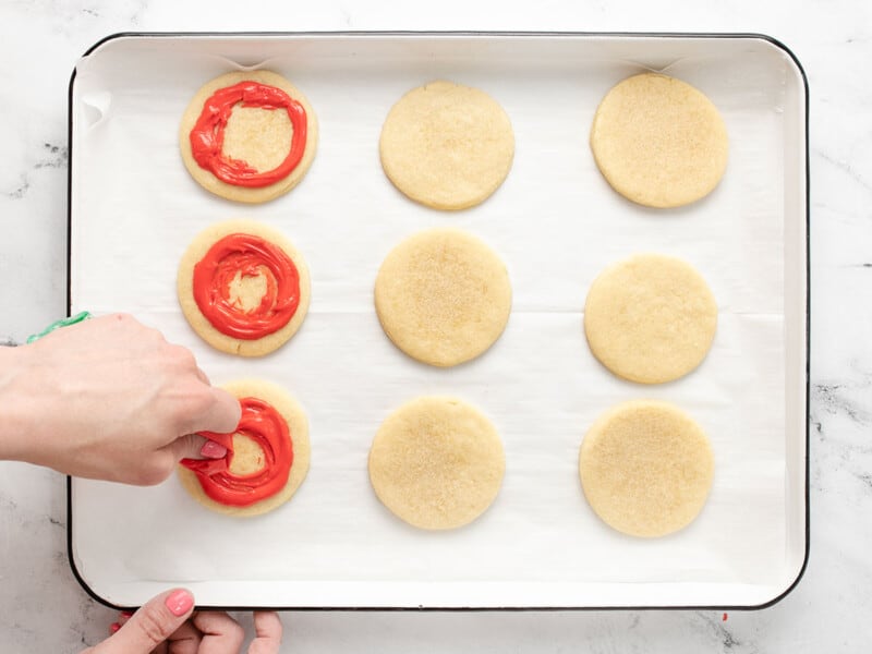 Overhead shot of hand piping icing onto a sugar cookie on a tray of sugar cookies.