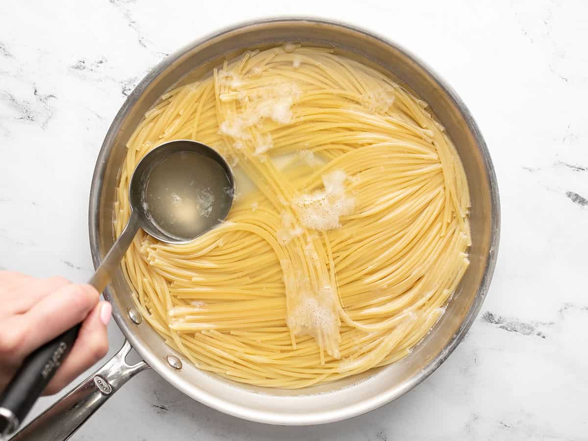 A ladle reserves pasta water from a pan of cooked spaghetti.