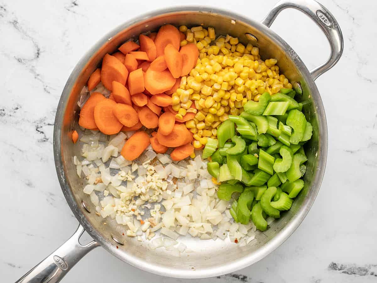 Overhead of diced onion, minced garlic, sliced carrots, celery and frozen uncooked in a skillet.