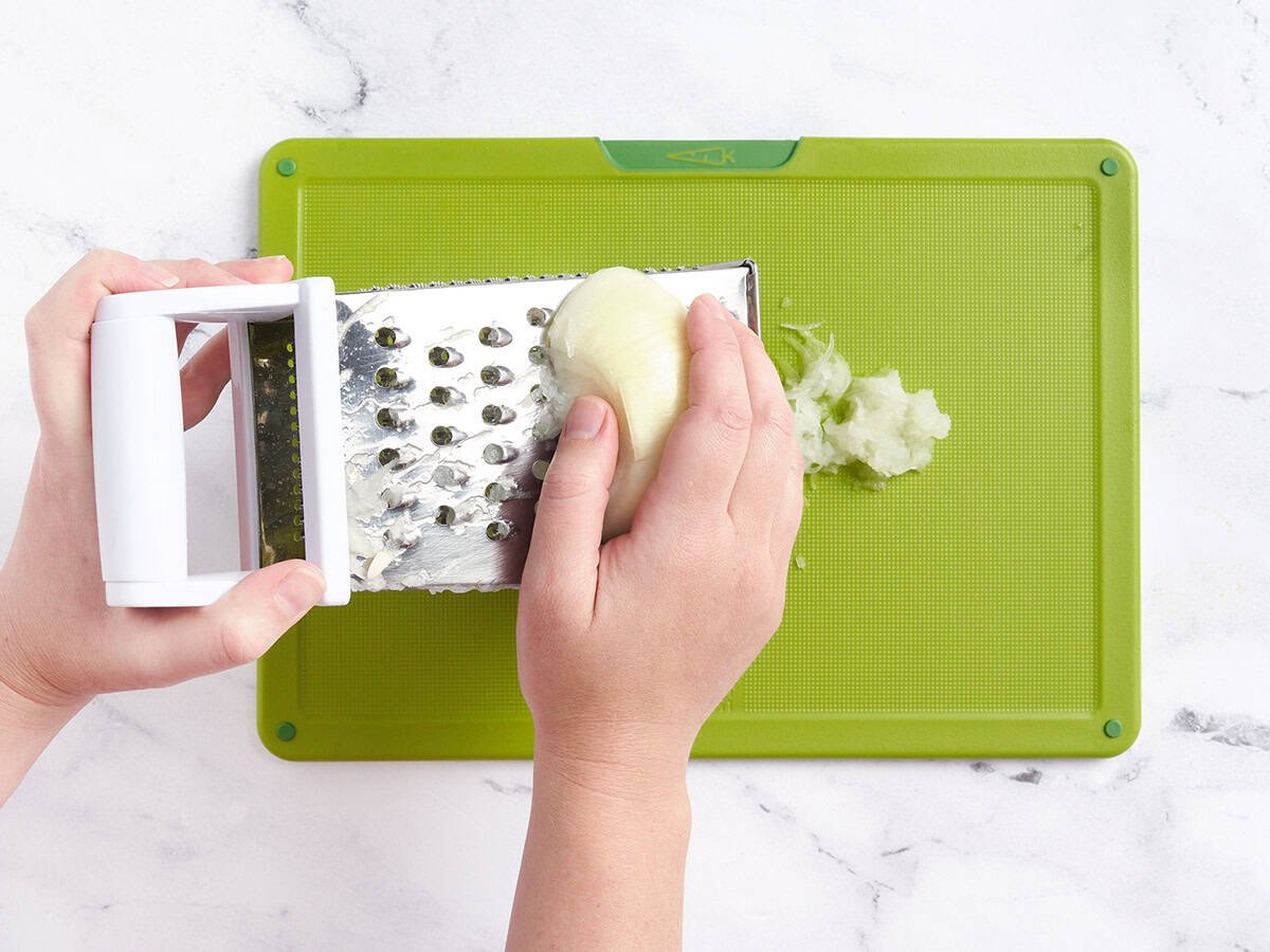 A hand using a cheese grater to grate an onion.