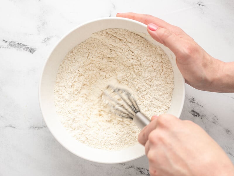 Overhead shot of hands mixing flour and baking powder in a white bowl.