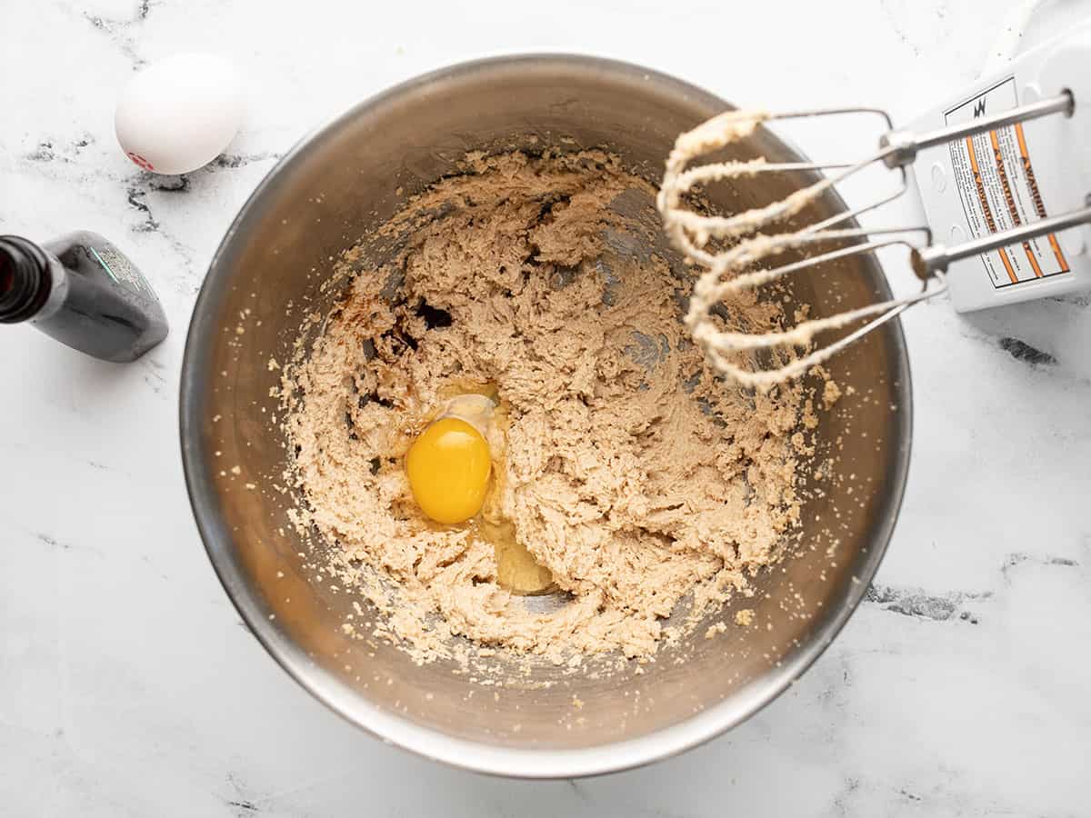 Overhead shot of eggs and vanilla in silver bowl with hand beaters settled on the rim..